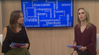as apresentadoras sentadas lado a lado, no meio delas um monitor de televisão com palavras escritas "diversidade" "saúde" "liberdade" "vida" "debate"